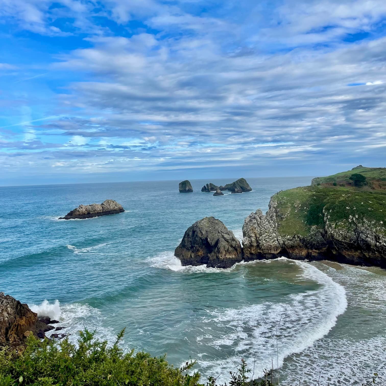 Vista aérea desde los acantilados de la Playa de Poo en Llanes, Asturias, mostrando su arena dorada, el oleaje del Cantábrico y los verdes prados que la rodean.