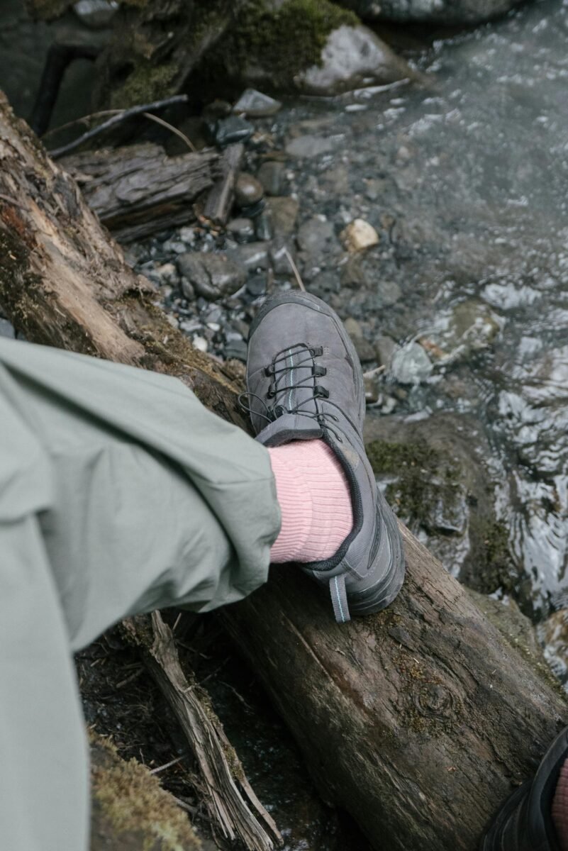 Close-up of a hiker's shoe on a log near a stream in a natural setting.